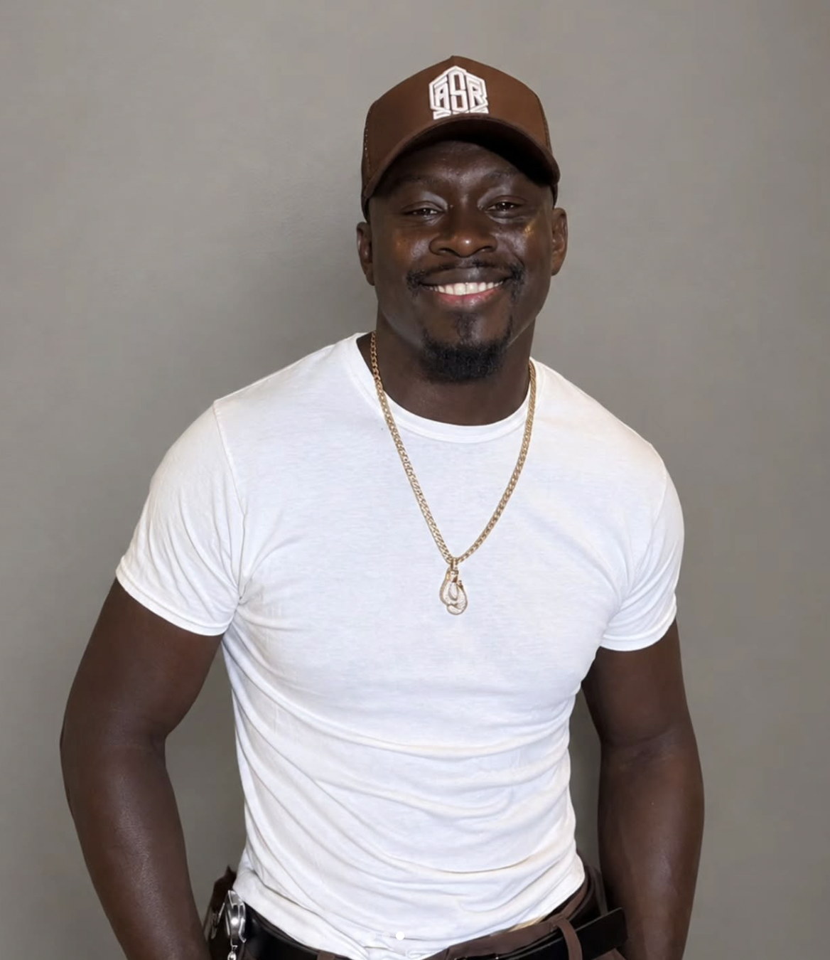 Curtis Millender smiling in a white shirt and brown cap